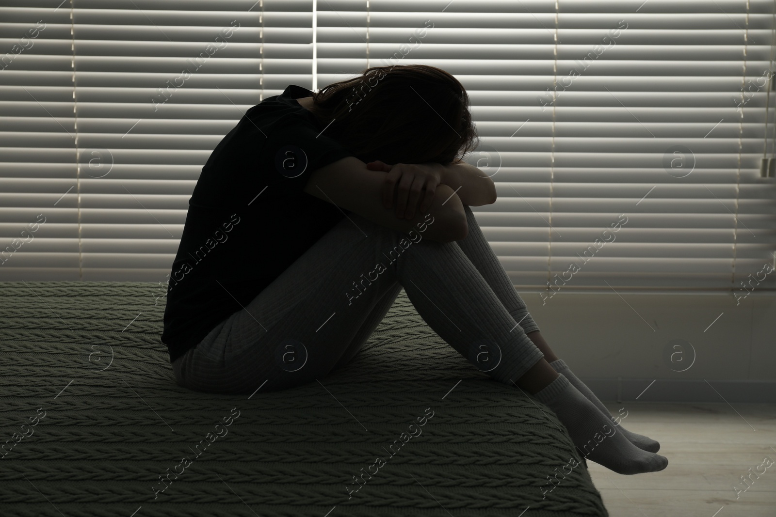Photo of Sad young woman sitting on bed at home