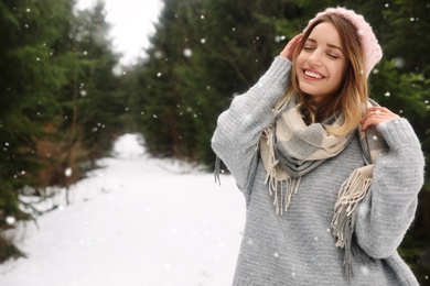 Young woman in snowy conifer forest, space for text. Winter vacation