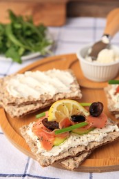 Photo of Fresh crunchy crispbreads with cream cheese, salmon, olives, lemon and green onion on table, closeup