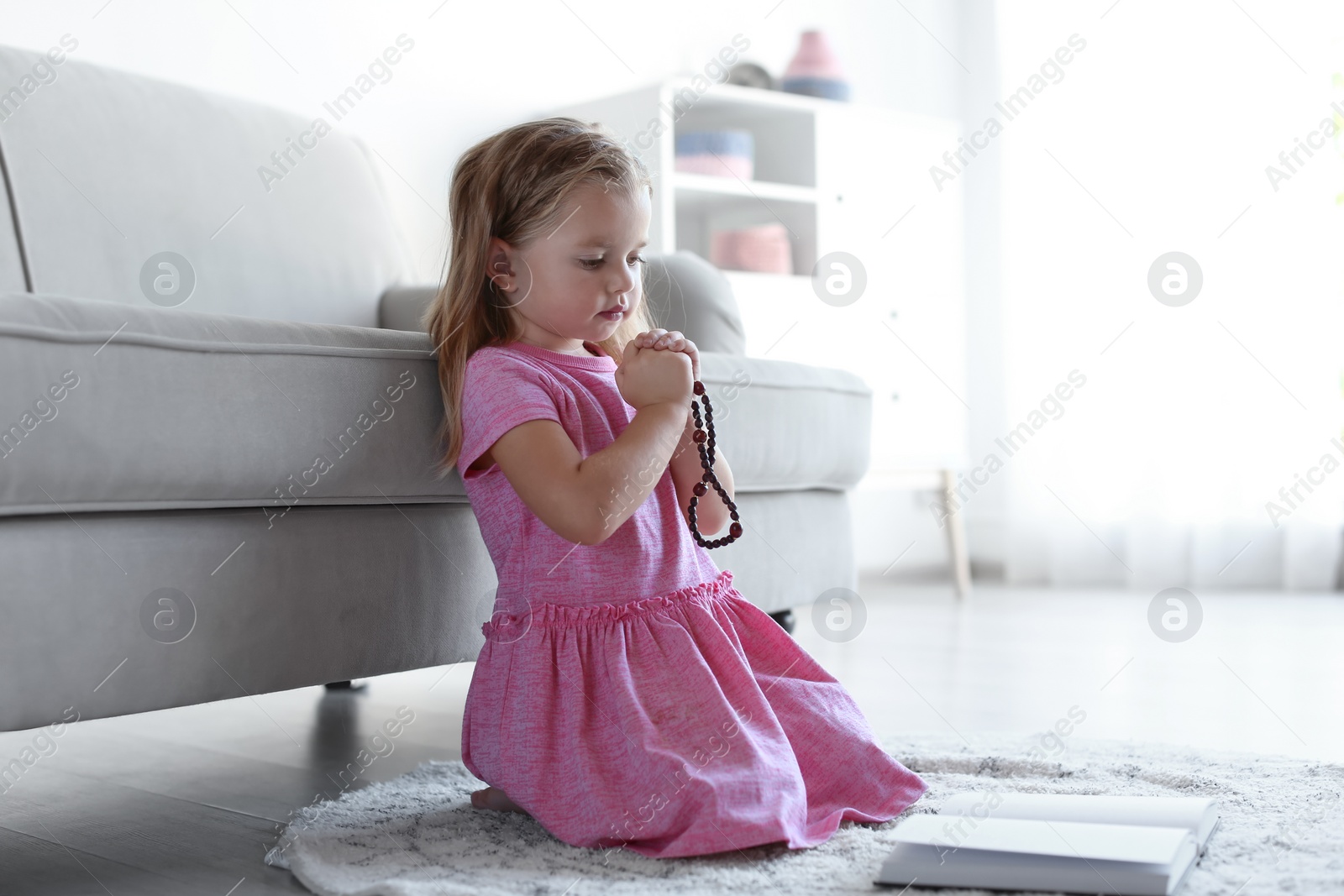 Photo of Cute little girl with beads praying in living room. Space for text