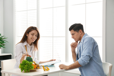 Photo of Young nutritionist consulting patient at table in clinic