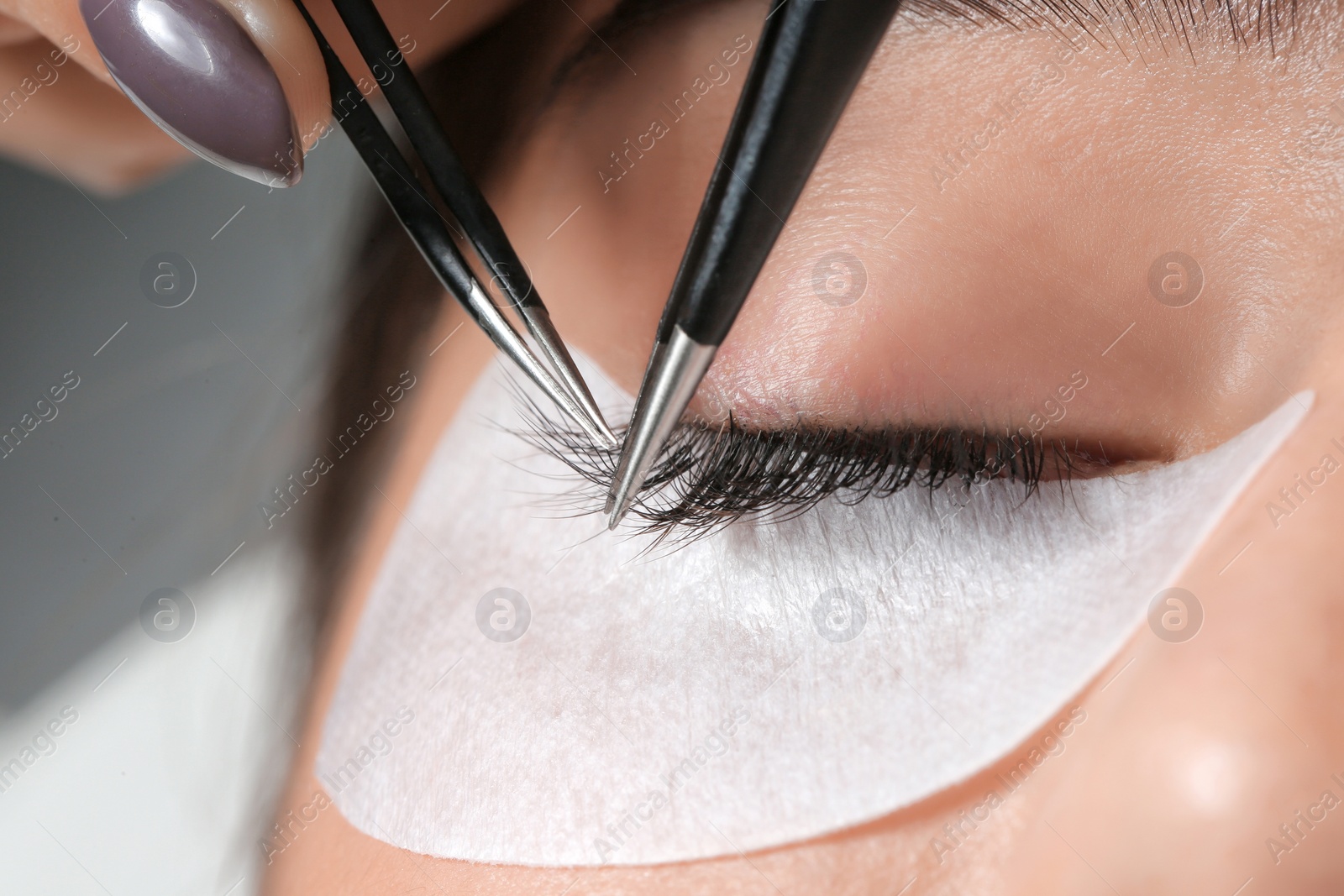 Photo of Young woman undergoing eyelashes extensions procedure, closeup