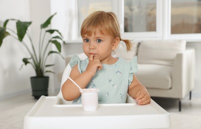 Photo of Cute little child eating tasty yogurt with spoon at home