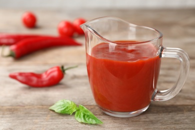 Jug with spicy chili sauce on wooden table