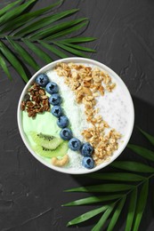 Photo of Tasty smoothie bowl with fresh kiwi fruit, blueberries and oatmeal on black table, flat lay