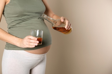 Photo of Pregnant woman pouring whiskey into glass on color background. Alcohol addiction