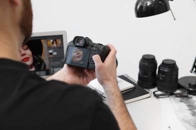 Photo of Professional photographer with digital camera at table indoors, closeup