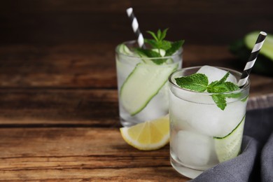 Glasses of refreshing cucumber water with mint on wooden table, space for text