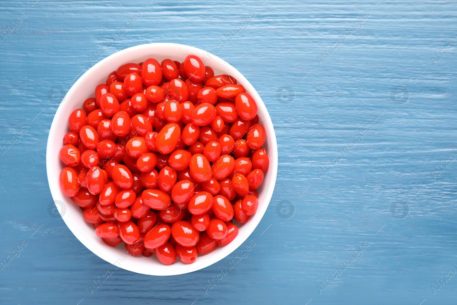 Photo of Fresh ripe goji berries in bowl on blue wooden background, top view. Space for text