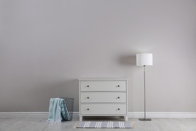 Stylish room interior with white chest of drawers, floor lamp and metal basket