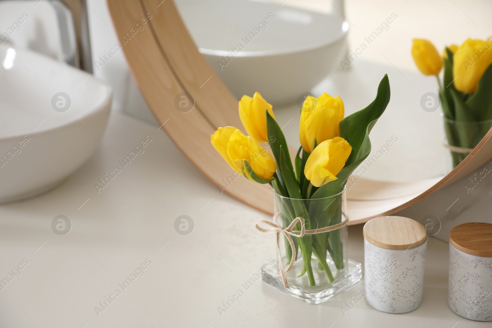 Photo of Beautiful yellow tulips near mirror on white table