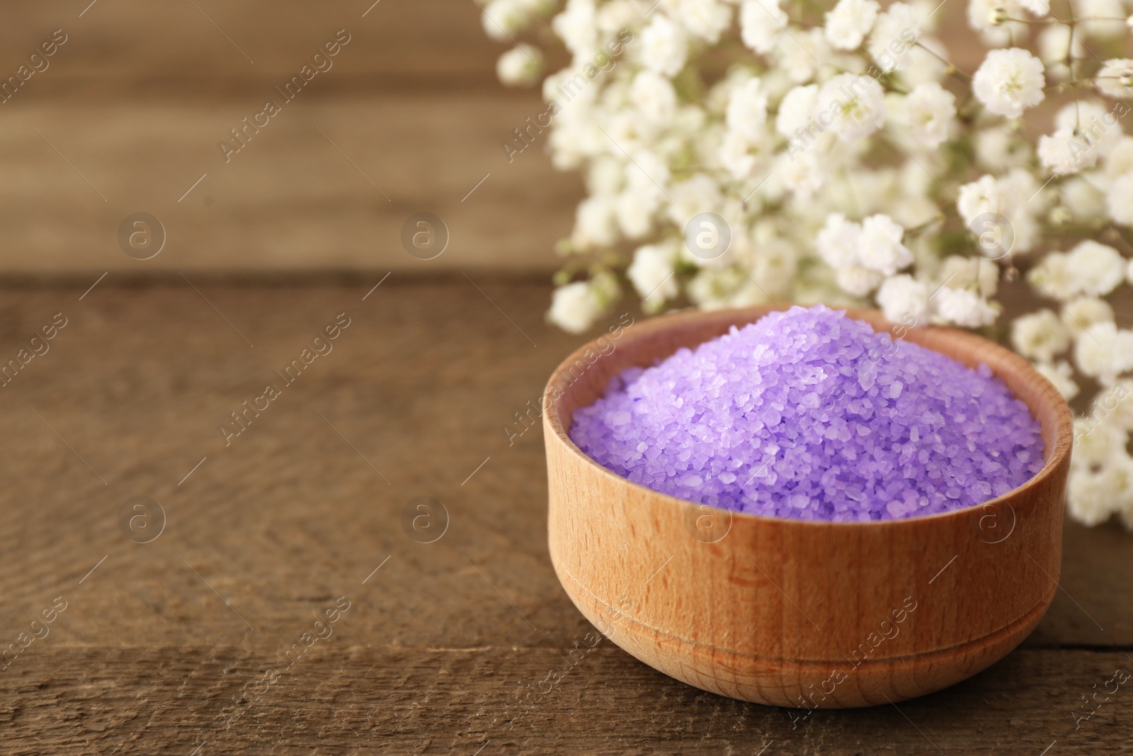Photo of Purple sea salt and beautiful flowers on wooden table, closeup. Space for text