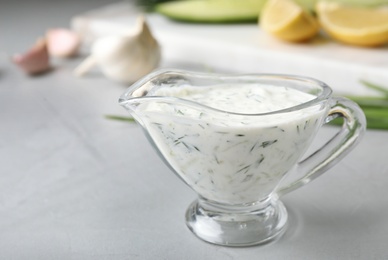 Photo of Glass gravy boat with cucumber sauce on grey table. Space for text