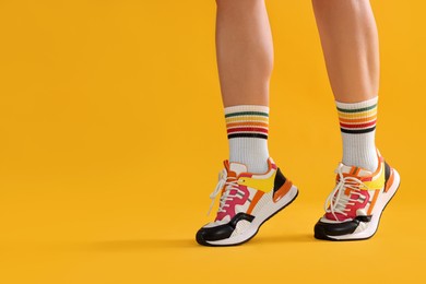 Photo of Woman wearing stylish sneakers on yellow background, closeup. Space for text