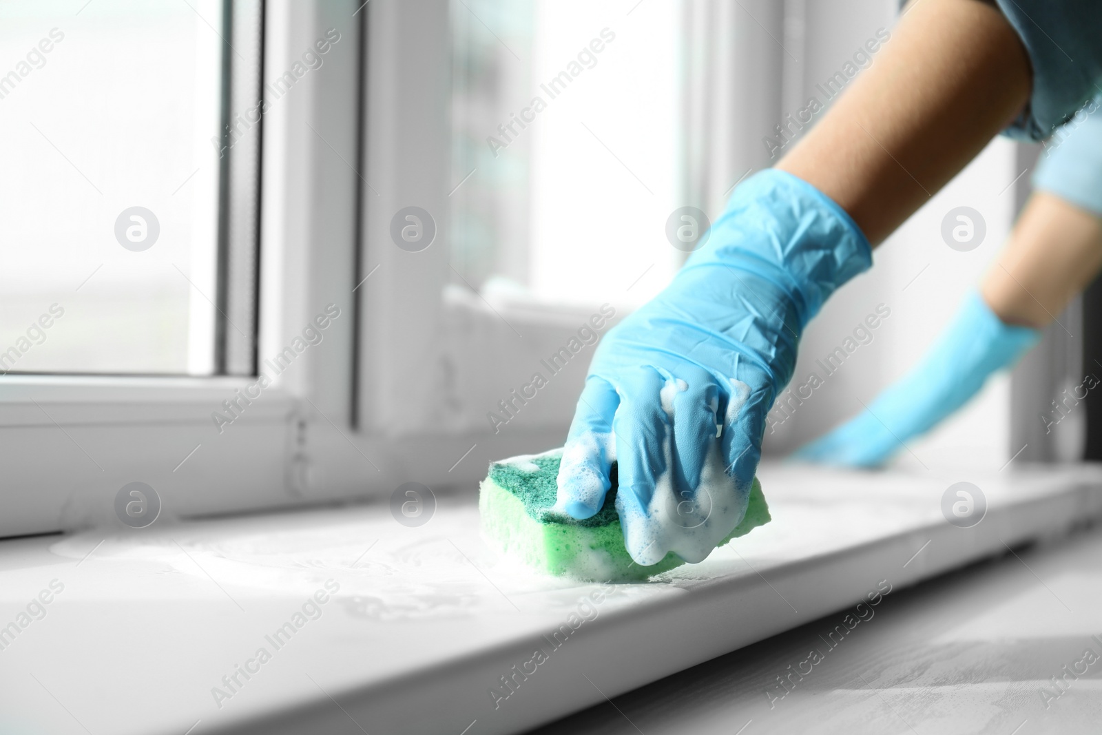 Photo of Woman cleaning window sill with sponge, closeup