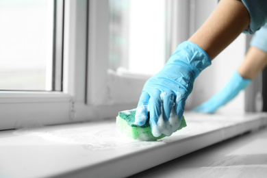 Woman cleaning window sill with sponge, closeup