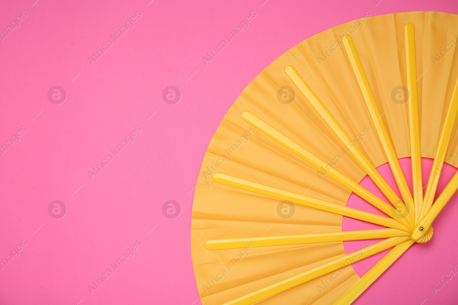 Photo of Bright yellow hand fan on pink background, top view. Space for text