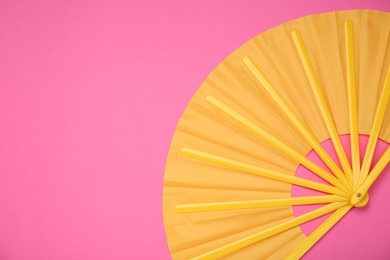 Bright yellow hand fan on pink background, top view. Space for text