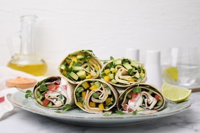 Delicious sandwich wraps with fresh vegetables and slice of lime on white marble table