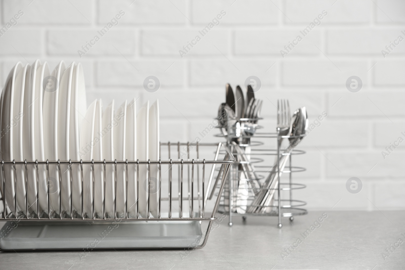 Photo of Dish rack with clean plates on table near brick wall. Space for text