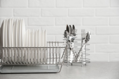 Dish rack with clean plates on table near brick wall. Space for text