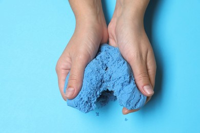 Woman playing with kinetic sand on light blue background, top view