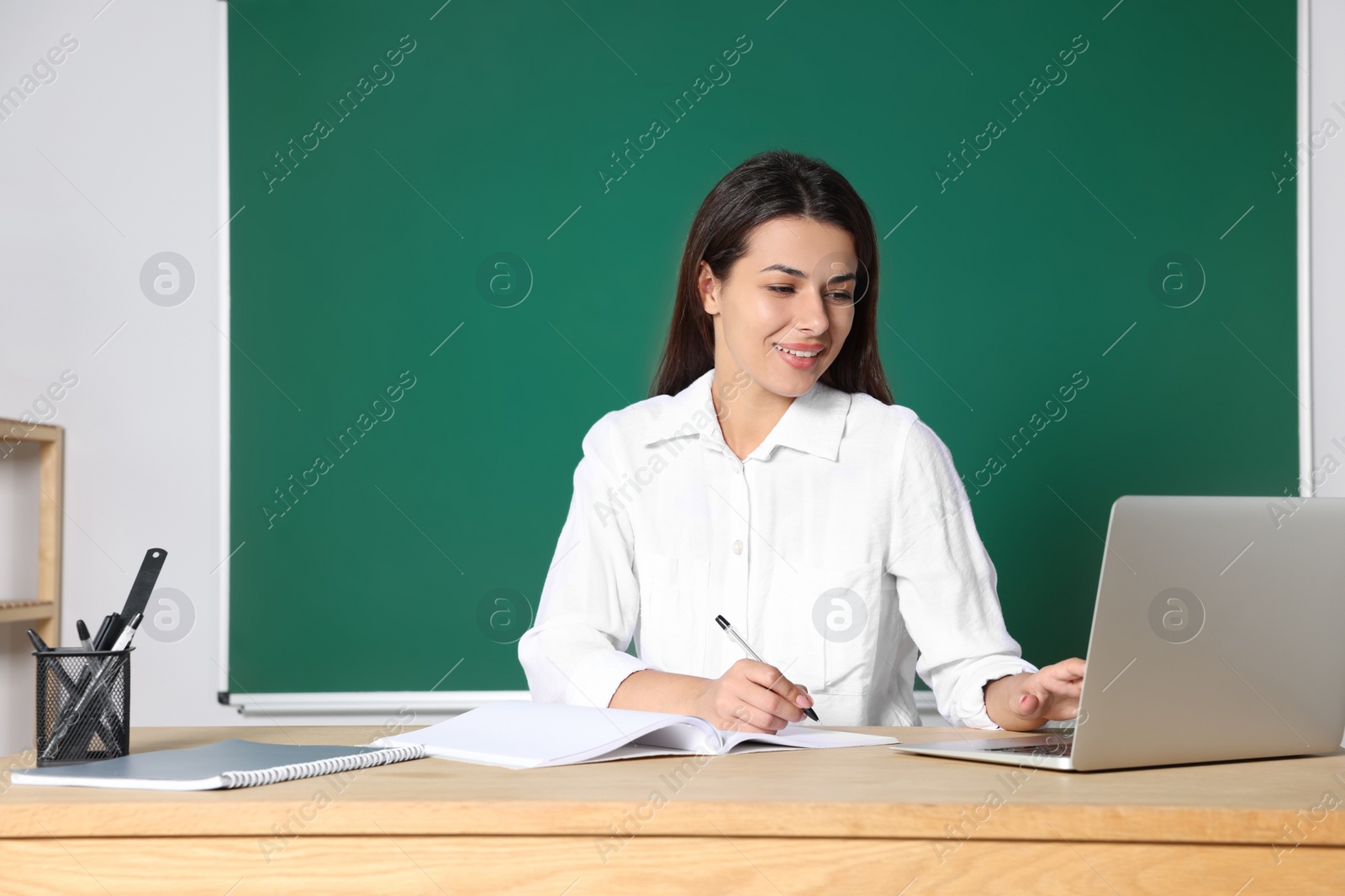 Photo of Young teacher giving lesson at table in classroom