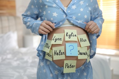 Pregnant woman with different baby names on belly in bedroom, closeup