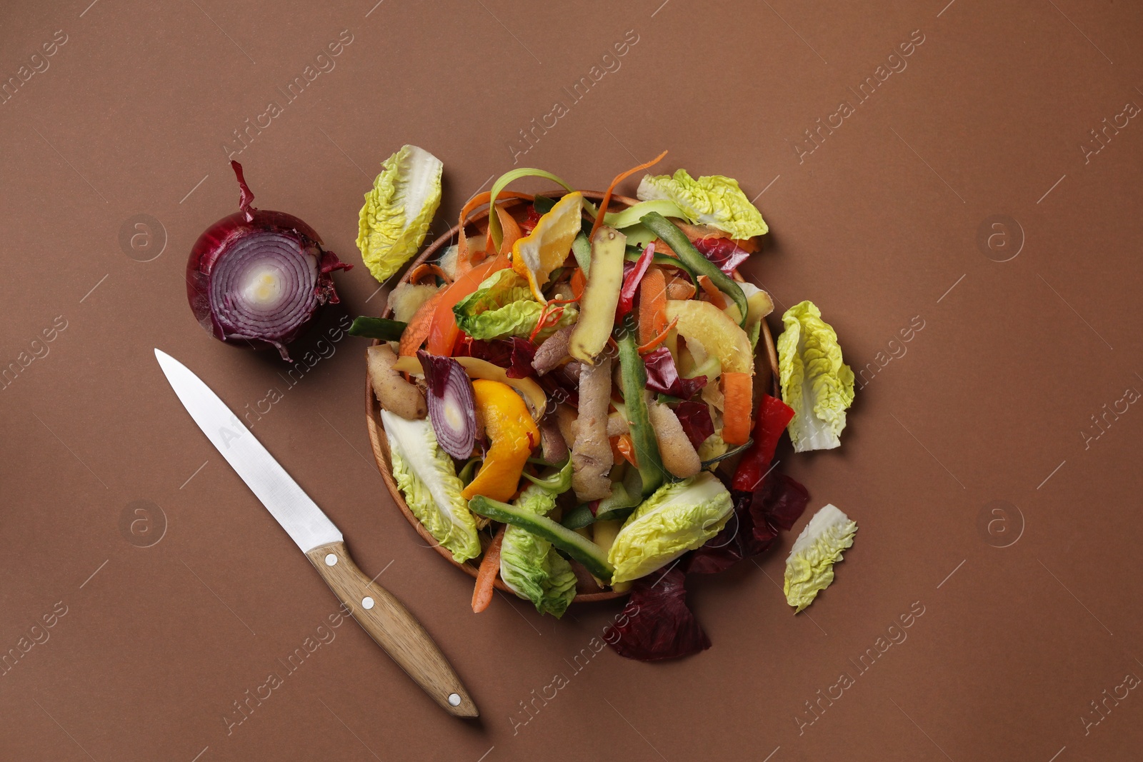 Photo of Peels of fresh vegetables and knife on brown background, flat lay