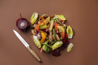 Peels of fresh vegetables and knife on brown background, flat lay