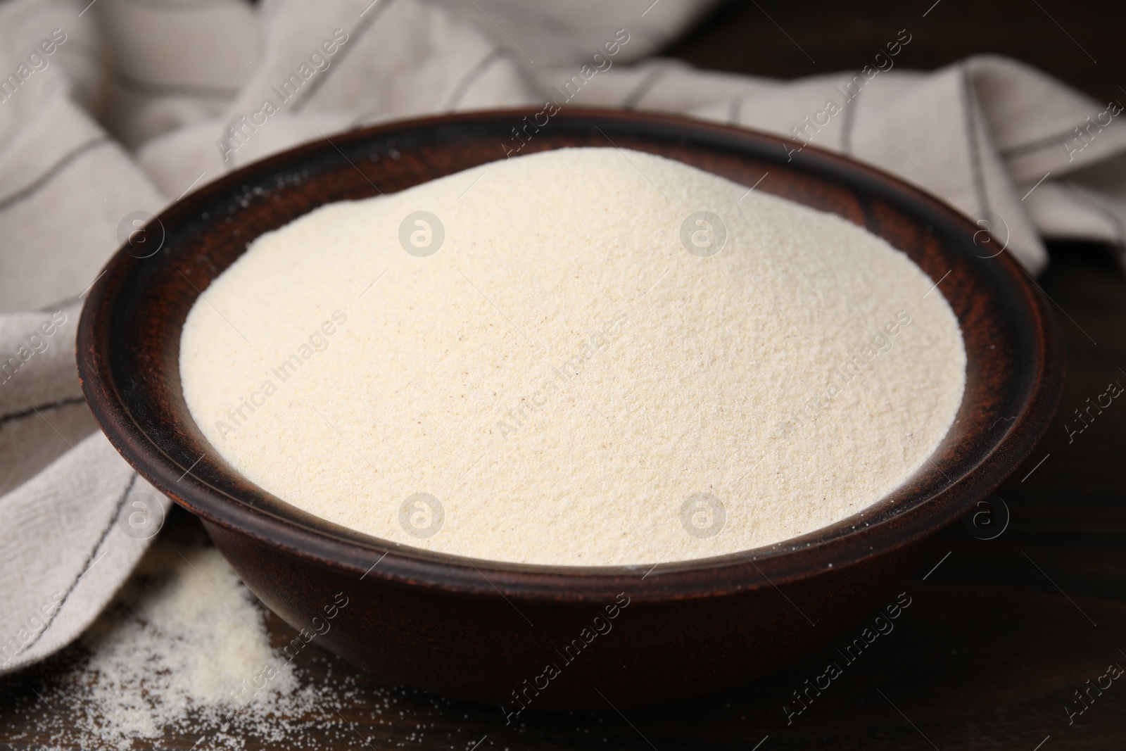 Photo of Uncooked organic semolina in bowl on wooden table, closeup