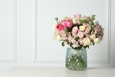 Photo of Beautiful bouquet of fresh flowers in vase on table near white wall. Space for text