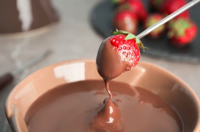 Photo of Ripe strawberry dipping into chocolate fondue, closeup