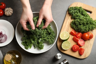 Photo of Woman cooking tasty kale salad on grey table, top view