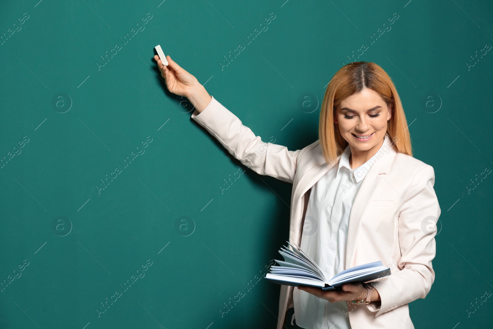 Photo of Beautiful teacher with book pointing at chalkboard, space for text