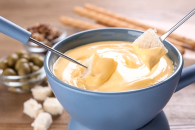 Dipping bread into pot with cheese fondue on table, closeup