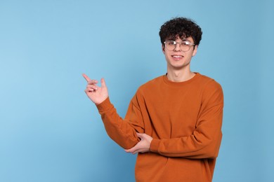 Handsome young man pointing at something on light blue background. Space for text