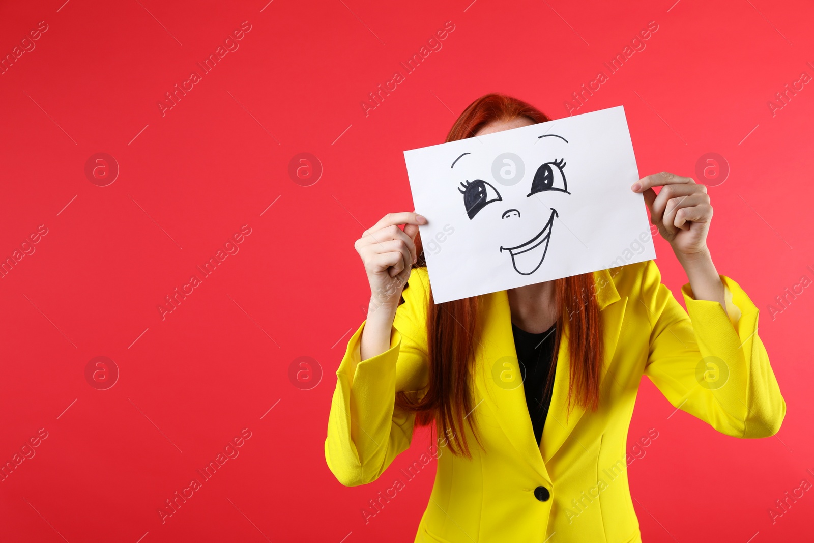 Photo of Woman hiding behind sheet of paper with happy face on red background, space for text