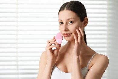 Photo of Washing face. Young woman with cleansing brush indoors, space for text