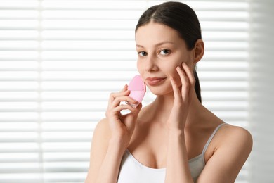 Washing face. Young woman with cleansing brush indoors, space for text