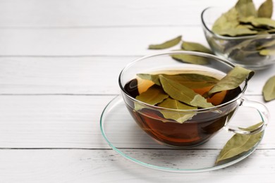 Cup of freshly brewed tea with bay leaves on white wooden table, closeup. Space for text
