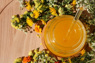 Photo of Delicious fresh honey in glass jar and beautiful flowers on wooden table, flat lay