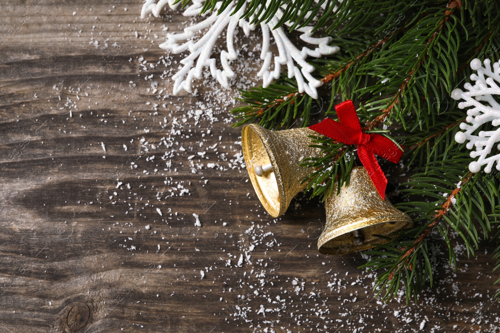 Photo of Christmas bells and fir tree branches with festive decor on wooden table, flat lay. Space for text