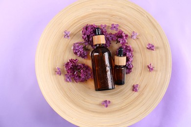 Photo of Tray with cosmetic products and lilac flowers on violet background, top view