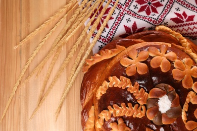 Rushnyk with korovai, wheat spikes on wooden table, flat lay. Ukrainian bread and salt welcoming tradition