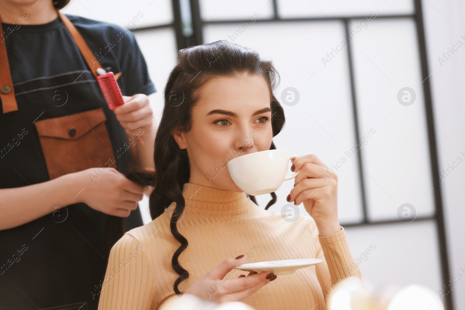 Photo of Hair styling. Professional hairdresser working with woman while she drinking coffee in salon, closeup