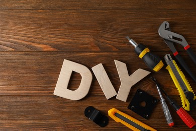 Photo of Abbreviation DIY made of letters and different tools on wooden table, flat lay. Space for text