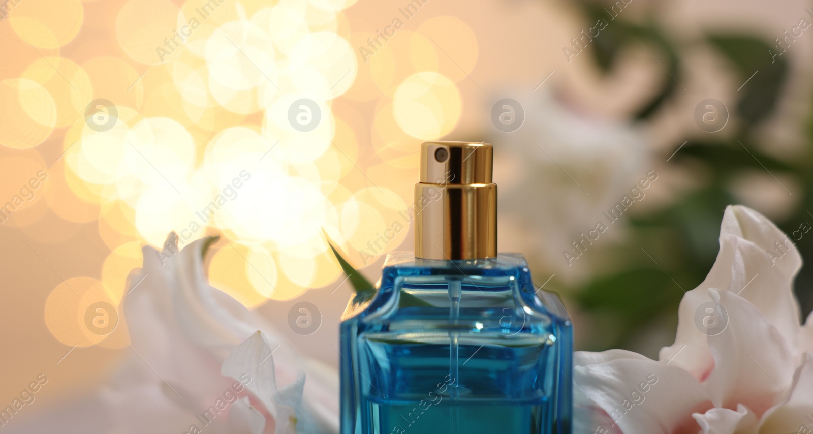 Photo of Bottle of perfume and beautiful lily flowers against beige background with blurred lights, closeup