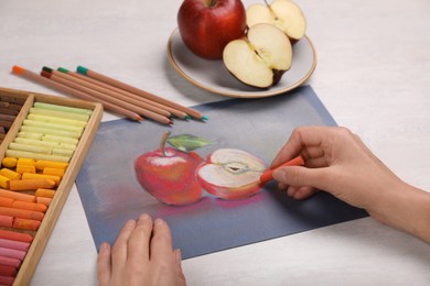 Photo of Woman drawing red apples on paper with soft pastels at white table, closeup