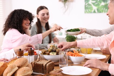 Photo of Friends eating vegetarian food at wooden table indoors